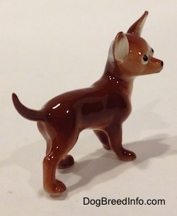 The back right side of a brown with white Chihuahua figurine. The figurine has fine paw details.